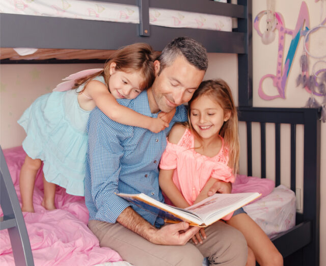 father reading a book to his young daughters